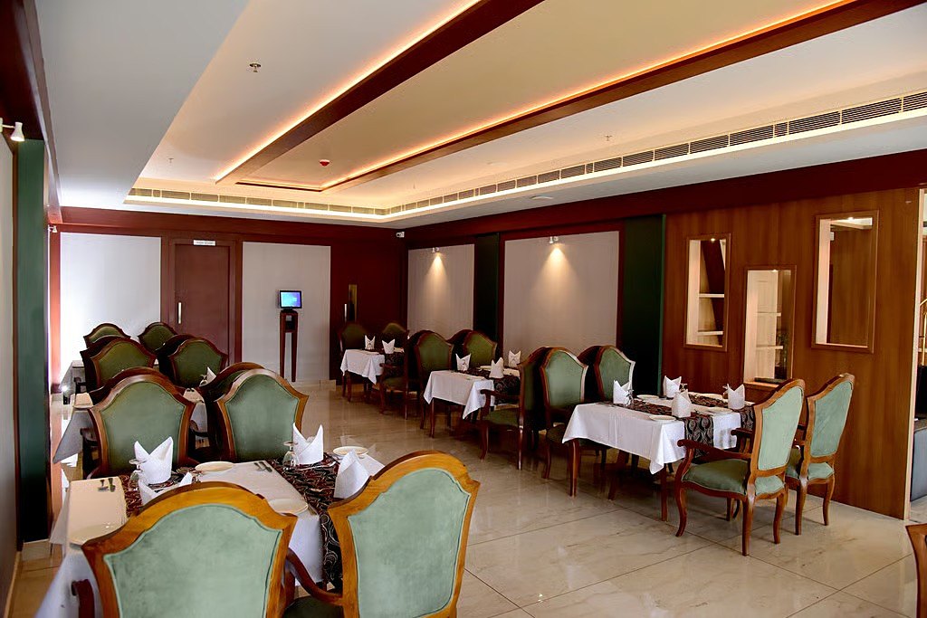 Amrit restaurant: tables in white linen, sage-green velvet chairs with carved teak frames and teak-panelled walls