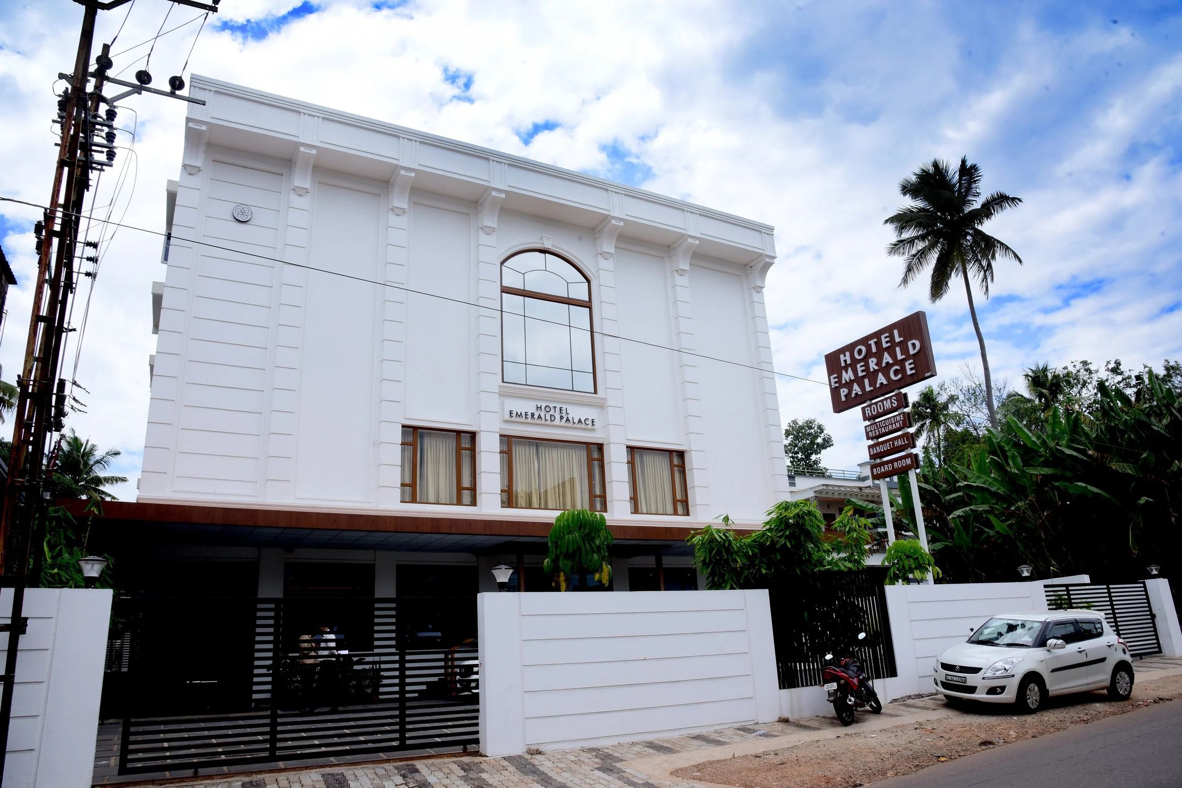 The white front of Hotel Emerald Palace, with its arched window, teak-framed windows and roadside sign, under a blue sky